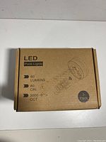 Closed brown cardboard box showing product details: LED Puck Lights, 80 Lumens, 80 CRI, 3000-6500K CCT, 3 Pack