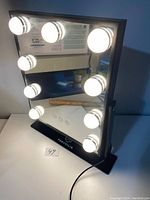 Front view of the rectangular LED vanity mirror on black stand, with 9 LED light bulbs illuminated around the mirror perimeter.