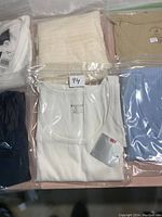 Photo showing a variety of ladies tops including cream knitted top, beige ribbed tank top, white tank tops, blue and black sleeveless tops neatly folded and packaged in plastic bags.