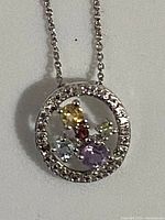 Close-up image of the round pendant showing colored gemstones and clear rhinestones around the circle edge.