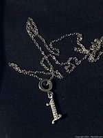 Silver chain necklace with a number '1' pendant and circular attaching charm lying on a black fabric background.