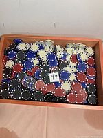 Photo showing a collection of red, black, blue, beige, and a few green poker chips inside a wooden tray with a handwritten '99' label on top.
