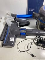 Vacuum cleaner parts including brush head, extension tubes, and charger with user manual on table.