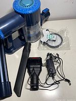 Blue handheld vacuum cleaner with dust container, two nozzle attachments, and charger adapter laid out on table.