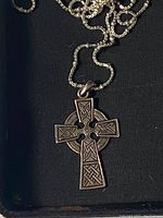 Close-up photo of the silver Celtic cross pendant showing detailed knotwork patterns on each arm and center circle, with partial view of chain.