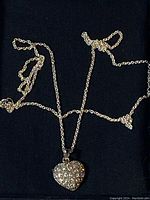 Silver-tone chain necklace laid flat with a heart-shaped rhinestone-encrusted pendant on a black background.