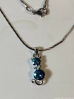Close-up of silver necklace with cat-shaped pendant having two blue stones and clear stone eyes on a table.