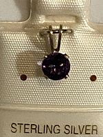 Close-up of a sterling silver pendant with a round amethyst stone mounted with prongs and attached to a bail.