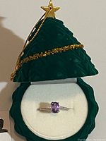 Ring with oval amethyst gemstone in green Christmas tree-shaped box with gold decoration.