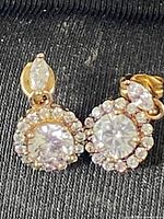 Pair of gold tone sterling silver earrings with marquise and round cubic zirconia stones sitting on a dark fabric background.