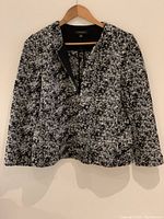 Front view of Ann Taylor ladies jacket in black and white knit with zip front, hung on wooden hanger against beige wall.