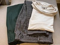 Three folded clothing items: soft oyster-colored cowl neck Banana Republic top, hunter green Zara pants, and grey/brown plaid Zara pants.