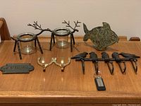 Photo of metal reindeer and fish tea light holders, brass equestrian hook, cast iron bird key holder, and 'Cuisine' door sign on wooden surface.