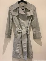 Front view of neutral color lightweight trench coat jacket with waist belt on hanger.