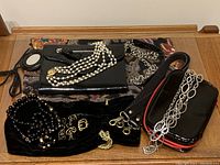 Wide view of the lot showing all items including bags, jewelry necklace draped over clutch, velvet pouches and straps on a wooden surface.
