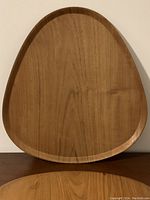 Front view of smooth wooden tray shaped like a guitar pick, showing wood grain and gently raised edges.