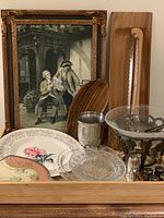 Overall shot showing framed vintage print, decorative plates, clear glass dishes, metal goblet, salt and pepper shakers and other assorted items on wooden tray