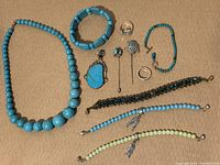 Wide shot of all jewelry pieces on a wooden surface showing turquoise necklace, beaded bracelets, silver rings, and pins.