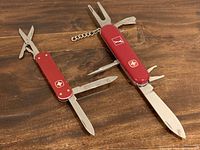 Top-down view showing both Swiss Army knives with tools open including blades, scissors, and golf divot tool on Wenger Golf Pro and money clip on Victorinox.