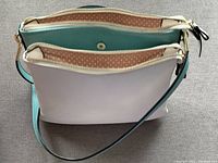View of two-tone vegan leather shoulder bag in light purple and turquoise with zipper tops and adjustable shoulder strap.