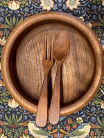 Top view showing the wooden salad bowl with wooden fork and spoon resting inside, highlighting the grain and shape.