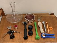 Full view of all items on display including the decanter, wine caddie, various bar tools, and kitchen utensils laid out on a wooden surface.
