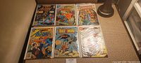 Top view of first set of 6 vintage comics including Superman Action Comics, Batman, and others in plastic bags.