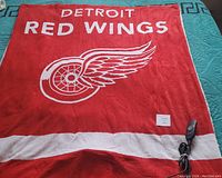 Full view of red Detroit Red Wings electric heating blanket spread out, showing logo, text, and controller unit.