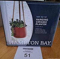 Front of the box showing the brand, item name, material, dimensions, and usage features with image of the planter hung with plants inside.