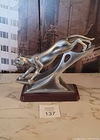 Front side view of metallic jaguar sculpture on wood base showing crouching pose and smooth metallic finish.
