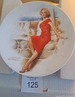 Front view of the Marilyn Monroe collectors plate showing her seated wearing a red dress with Niagara Falls in the background, signature of the artist visible.