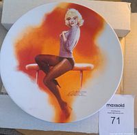 Front view of Marilyn Monroe collectors plate with artwork of Monroe sitting on a bench in stockings and sweater, displayed in original packaging box.