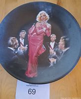 Front of a decorative plate showing Marilyn Monroe in pink dress with men around her.