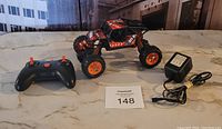 Photo showing the remote control off road vehicle, remote control, and battery charger on a countertop with a MaxSold auction card numbered 148
