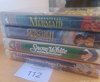 Side view of four sealed Walt Disney VHS tapes stacked horizontally showing spine titles: The Little Mermaid, The Little Mermaid II: Return to the Sea, Snow White and the Seven Dwarfs, The Hunchback of Notre Dame