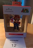 Front view of the Hallmark Super Mario Mario ornament in original packaging showing the character holding a mushroom and visible Super Mario and Hallmark branding.