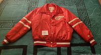 Front view of red satin Vintage Detroit Red Wings jacket with logo on chest and striped sleeves and cuffs.
