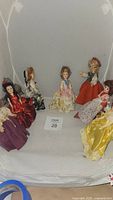 Seven vintage dolls arranged in a semicircle on white fabric background showing variety of costumes and colors.