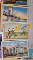 Photo showing multiple postcards laid out including a suspension bridge, a humorous moon-themed card, and a large building with flag.
