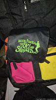 Close-up of backpack showing the bright yellow, pink, orange color paneling and the green logo with silhouette.