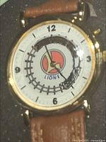 Close-up of the wristwatch face showing a train moving around the dial, gold-tone case and brown leather-like strap.