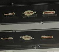 Eight Craftsman milestone collector's pins in two black display cases, each with four pins. Pins show anniversary years 1927, 1952, 1977, and 2002 with the Craftsman logo in various design styles.