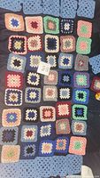 Crocheted squares in various colors and patterns laid out flat showing multiple rows of squares in different sizes.