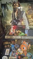 Photo showing a tall Pirates of the Caribbean poster with Captain Jack Sparrow and several plush toys including Tigger, a green plush, and a clownfish from Finding Nemo, plus buttons and pins spread out at the bottom.