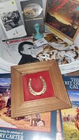 Western-themed books, magazines, framed gold horseshoe, and calendars arranged together.