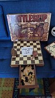 Photo of Pirates of the Caribbean Battleship game box, wooden chessboard with pull-out drawer containing chess pieces on a blue couch.