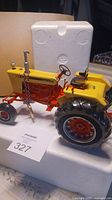 Side view of the yellow and red die cast Case 930 Comfort King tractor model with black rubber tires, positioned on white styrofoam box.