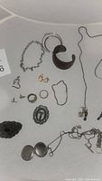 Overview of all jewelry items in lot including silver chain bracelet, copper cuff, J.Jill anklet, rings, earrings, locket and eyeglass chain.