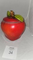 Front view of the large red apple-shaped ceramic cookie jar on a gray surface, showing the round body and lid with brown stem and green leaves.