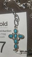 Close-up of silver-tone chain bracelet with turquoise stone cross pendant